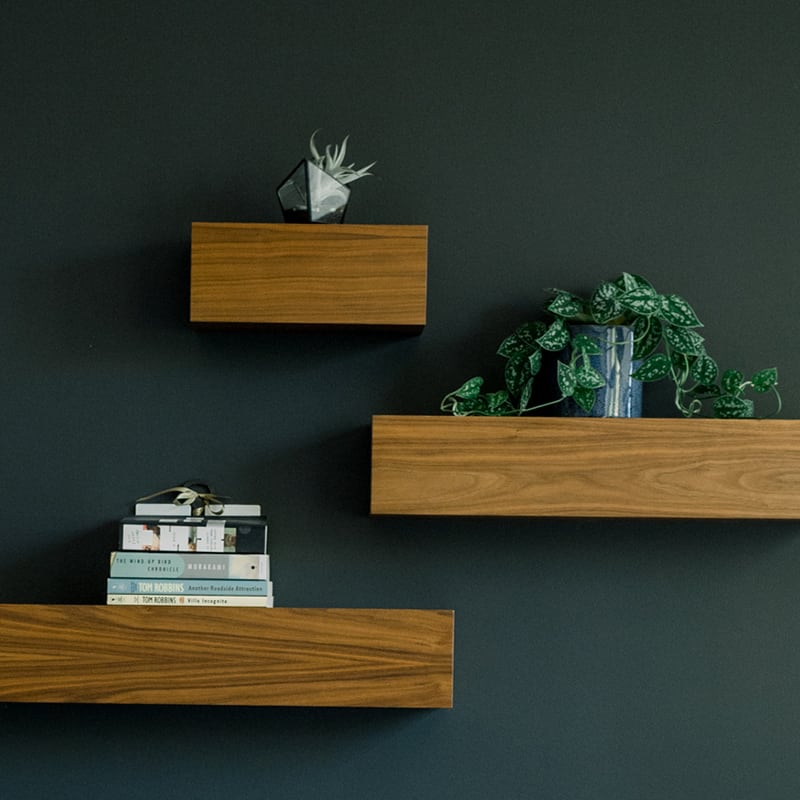 Three wooden shelves displaying books and plants, creating a harmonious blend of nature and knowledge.