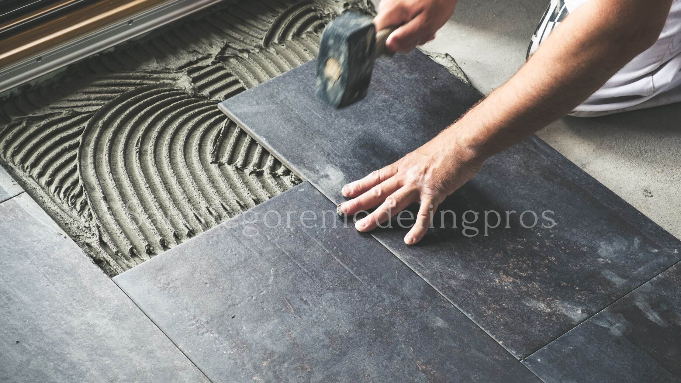A man carefully placing a tile on the floor, ensuring precise alignment and smooth installation. Best Flooring Option For Bathrooms
