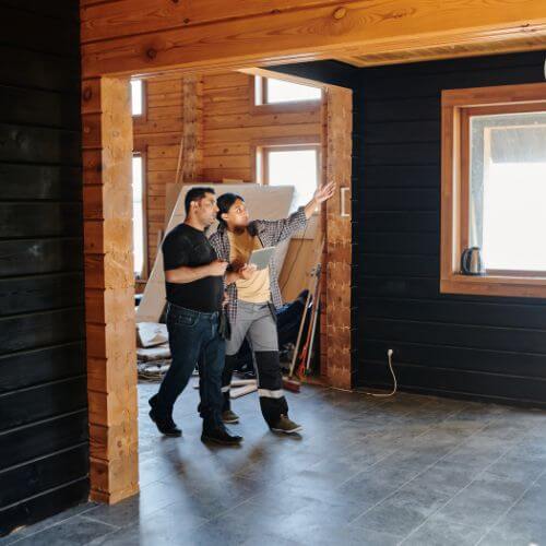 Two professionals stand together in a cozy room with warm wood walls, deciding on the interior of a room.