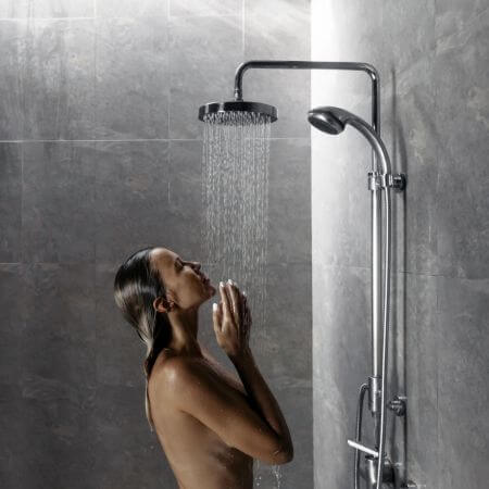 Shower-Remodeling-1 A woman stands in the shower with her arms raised, enjoying the water flowing down her body.